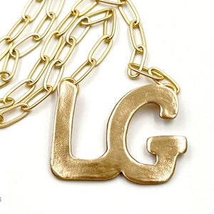 May include: A gold necklace with a toggle clasp and a large, chunky pendant featuring the letters "LG".