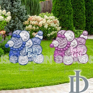 May include: Two white, silver, and blue poodle-shaped yard signs with the text "Baby Boy" and "Baby Girl" on them. The signs are on a green lawn.