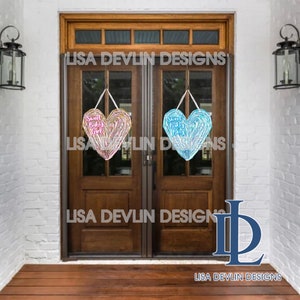May include: Two heart-shaped door hangers with the text "Sweet Baby Girl" and "Sweet Baby Boy" in pink and blue glitter lettering. The hangers are hanging on a wooden door with a glass pane.