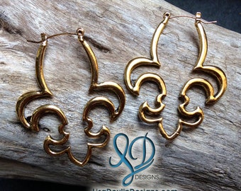 May include: A pair of gold-toned hoop earrings with a decorative fleur-de-lis design. The earrings are made of metal and have a shiny finish.