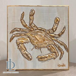 May include: A gold-painted crab sculpture on a white background. The crab is textured and has a three-dimensional appearance. The artist's signature, "L. Devlin", is in the bottom right corner.