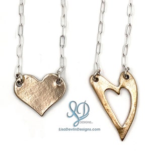 May include: Two gold heart necklaces on silver chains. One heart is solid and the other has a cut-out heart shape.