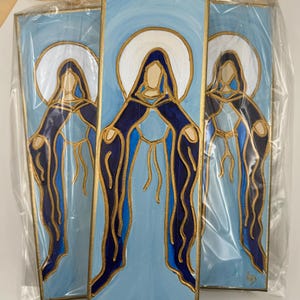 May include: Three blue and gold painted wooden plaques with a stylized image of a woman in a blue robe and a white halo. The plaques are wrapped in clear plastic and have a gold border.