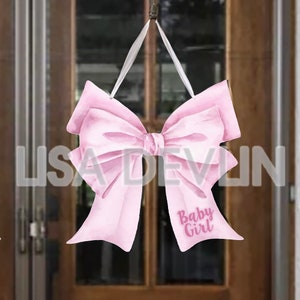 May include: A pink bow-shaped sign with the text "Baby Girl" in a script font. The sign is suspended by a white ribbon. The name "LISA DEVLIN" is printed in large, transparent letters.