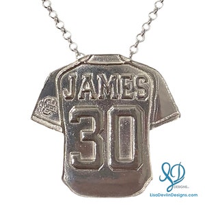 May include: Silver necklace with a baseball jersey pendant. The jersey has the name "JAMES" and the number "30" on it.