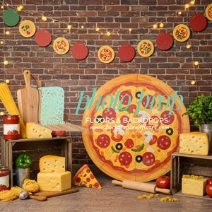 May include: A pizza-themed backdrop with a brick wall background. The scene includes a large pizza, wooden crates with cheese and tomatoes, pasta, and a garland of pizza and tomato decorations. A rolling pin and cutting boards are also present.