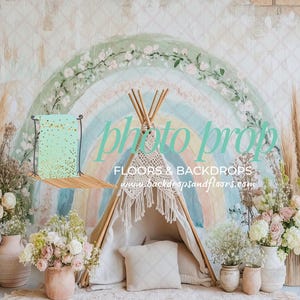 May include: A photo prop backdrop featuring a hand-painted rainbow design with a teepee, flowers, and pampas grass. The backdrop includes a small shelf with a mint green surface and gold accents. The words "photo prop" are visible.