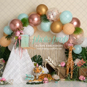 May include: A photo prop backdrop with a balloon arch in gold, peach, and teal. A white teepee, a toy tiger, and a giraffe are in the foreground. The backdrop includes floral and greenery accents.