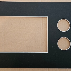 May include: Black mount board with a white border and two circular cutouts. The mount board is designed for framing a picture or artwork.