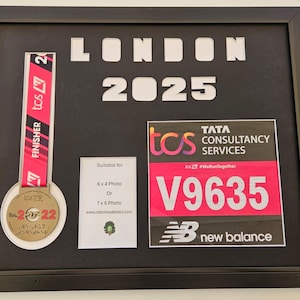 May include: A framed display of a marathon finisher's medal and race bib. The medal is gold with a blue ribbon and the text "London 2022". The race bib is pink and white with the text "TCS Tata Consultancy Services" and "V9635".