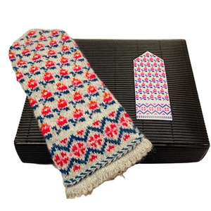 May include: A pair of knitted mittens with a white background and a colorful geometric pattern in shades of pink, red, blue, and orange. The mittens are displayed on a black mat with a matching bookmark.