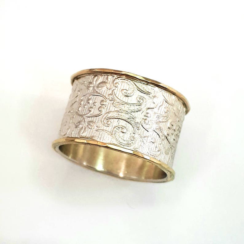 May include: A wide silver ring with an engraved floral pattern. The ring has gold-colored edges, creating a two-tone effect. The ring is approximately 0.75 inches wide.