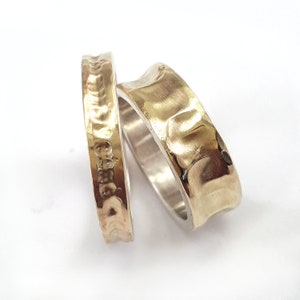 May include: Two gold rings, one with a hammered texture and the other with a smooth, rounded surface. The rings are stacked on top of each other.