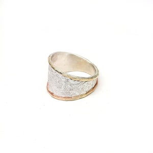 May include: A silver ring with a textured design and a gold band.