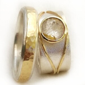 May include: Two rings: one with a hammered gold band and silver exterior, the other with a gold-rimmed gemstone set in a silver band with gold accents. The gemstone has inclusions.