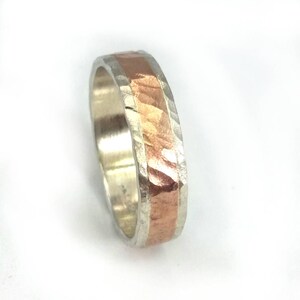 May include: A silver and copper band ring with a hammered texture. The copper band is set into the silver band.