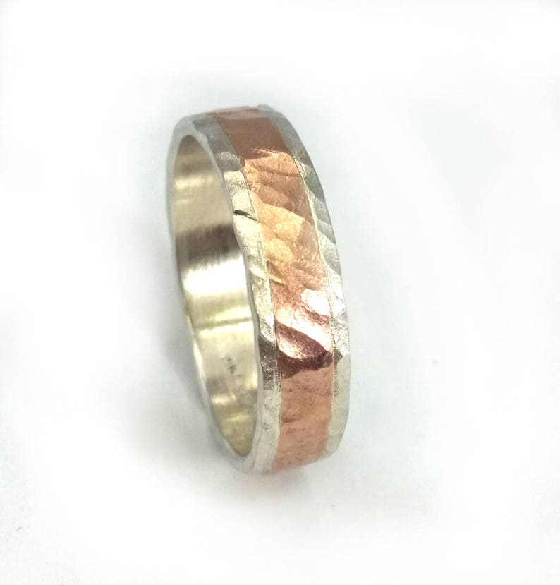 May include: A silver and copper band ring with a hammered texture. The copper band is set into the silver band.