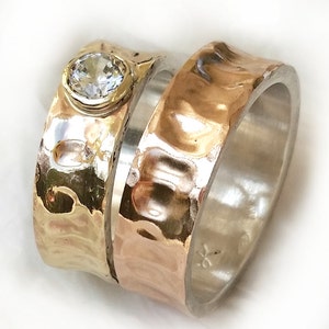 May include: Two hammered metal rings, one silver and one gold, with a clear gemstone set in the gold ring.