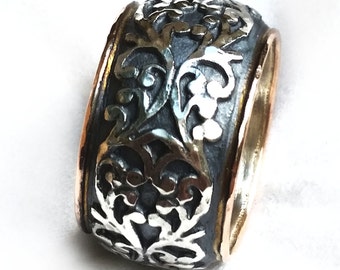 May include: A wide silver band ring with a decorative design of stylized leaves and flowers. The ring has a thin band of gold around the edge.