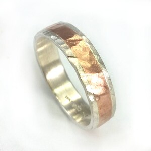May include: A silver band with a hammered texture and a thin band of copper running along the top. The band is marked "18K".
