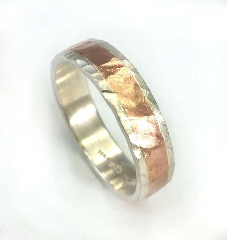 May include: A silver band with a hammered texture and a thin band of copper running along the top. The band is marked "18K".