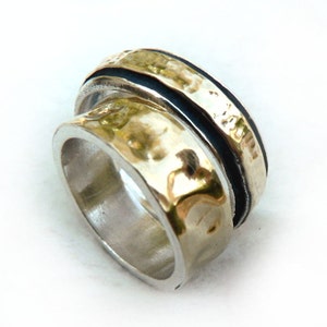 May include: A silver ring with a hammered gold band and a black band. The ring has a unique, textured design and a polished finish. The ring is a statement piece, suitable for everyday wear or special occasions.