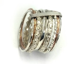 May include: A silver ring with multiple bands, some with textured designs, and two thin bands of rose gold.