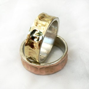 May include: Two hammered metal rings, one gold and one copper, stacked on top of each other. The gold ring has a textured surface and the copper ring has a smooth surface.