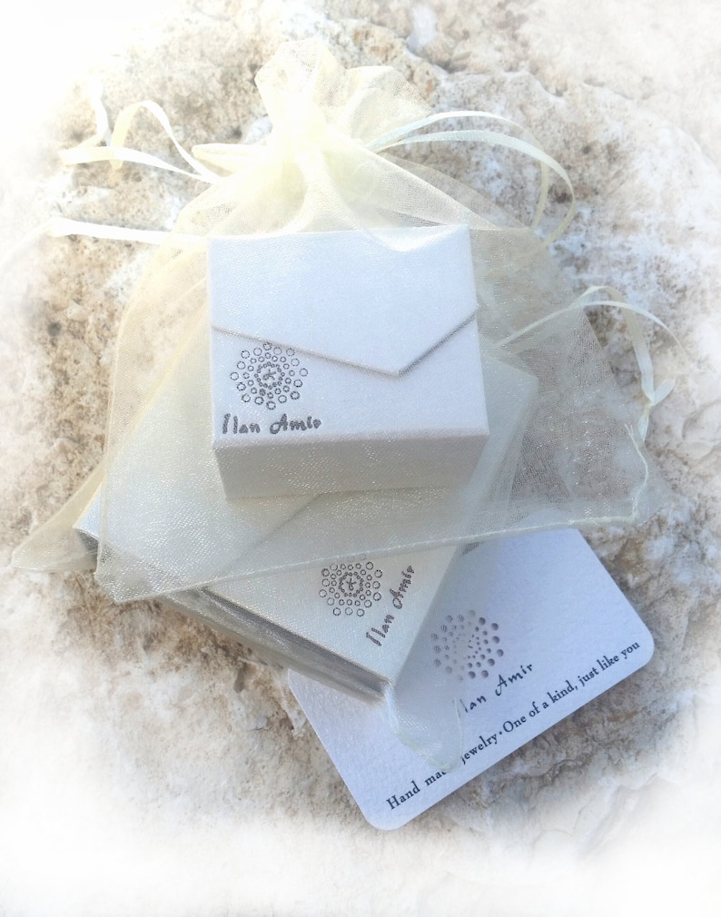 May include: A white box with a logo that says "Ilan Amir" and a white card with the text "Hand made jewellery. One of a kind, just like you" and the logo "Ilan Amir".