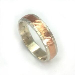 May include: A silver and copper band ring with a hammered texture. The ring has a copper band in the centre and is marked with the text "K 520 1/2".