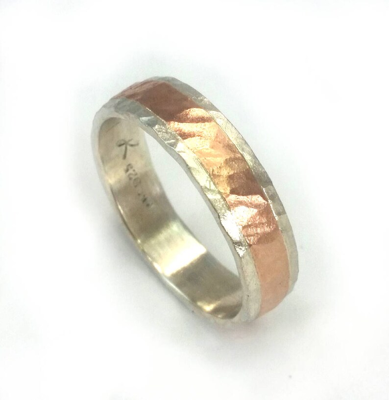 May include: A silver and copper band ring with a hammered texture. The ring has a copper band in the centre and is marked with the text "K 520 1/2".