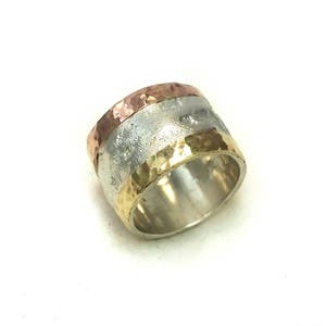以下が含まれることがあります： 金と銅の3つのバンドが付いた、ハンマーで叩いた質感の銀のリングです。