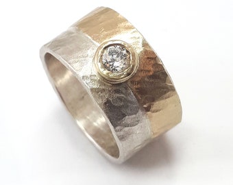 May include: A silver and gold band ring with a single round diamond set in a bezel setting. The ring has a hammered texture.