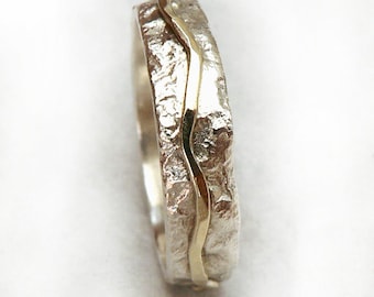 Puede incluir: Un anillo de plata con una banda de oro ondulada. El anillo tiene una superficie texturizada.
