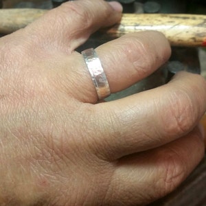 May include: A silver hammered band ring worn on a finger.