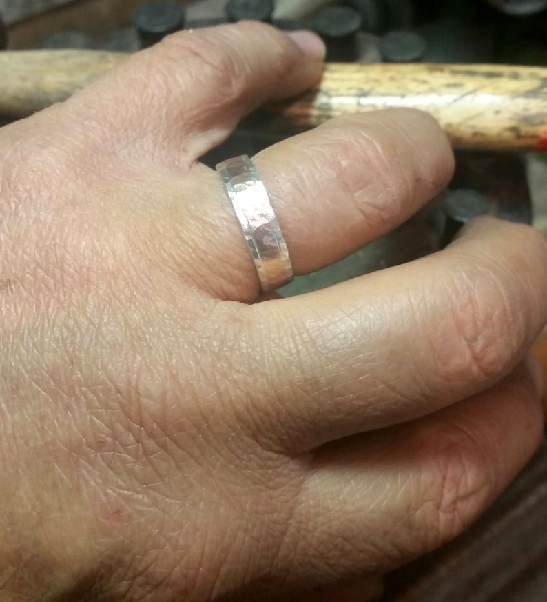 May include: A silver hammered band ring worn on a finger.