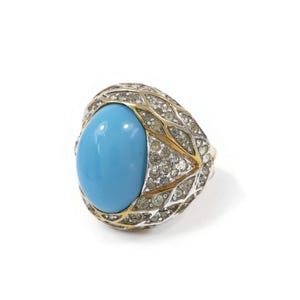 Peut inclure: Une bague en turquoise avec un sertissage en or et argent. La bague est sertie de petites pierres claires autour de la pierre précieuse.