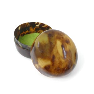May include: An oval trinket box with a tortoiseshell pattern. The lid is open, revealing a light green interior. The box is made of a dark brown material with a glossy finish.