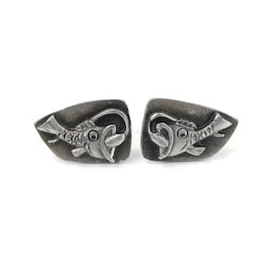 May include: A pair of silver cufflinks featuring a detailed design of a fish with an open mouth. The fish is depicted in a stylised, almost cartoonish manner.