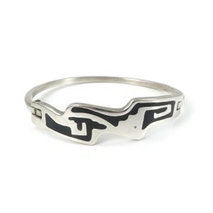 Peut inclure: Un bracelet jonc articulé en argent avec une finition métallique lisse et une incrustation noire contrastante. Le design présente un motif géométrique abstrait avec des lignes nettes et angulaires qui enveloppent l'avant du bracelet.