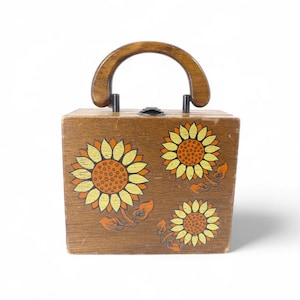 May include: A vintage wooden box handbag with a curved wooden handle. The box is decorated with three sunflowers in yellow, orange, and brown. The handbag has a small metal clasp and is likely from the mid-20th century.