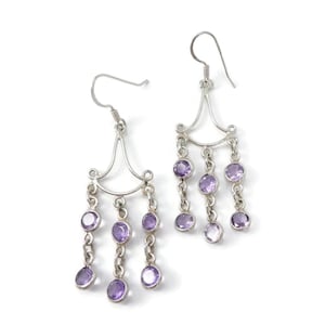 Peut inclure: Une paire de boucles d'oreilles chandelier argentées avec trois chaînes pendantes, chacune ornée de petites pierres rondes de couleur améthyste serties dans des chatons en métal. Les boucles ont des crochets incurvés pour la fixation.