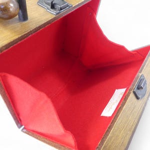 May include: A wooden box-style handbag with a hinged lid and a dark metal latch closure. The interior is lined with bright red fabric and features a small white rectangular tag with the text Marcus Brothers Made in England printed in black.