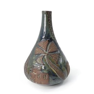 May include: A teardrop-shaped ceramic vase with a glossy dark blue and green glaze. The surface features embossed brown clay details depicting a palm tree and a small building structure, with geometric patterns along the narrow neck.