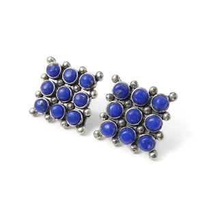 May include: A pair of square stud earrings with a grid of twelve deep blue stones in each. The stones are set in a silver-coloured metal. The earrings have a vintage or antique appearance.
