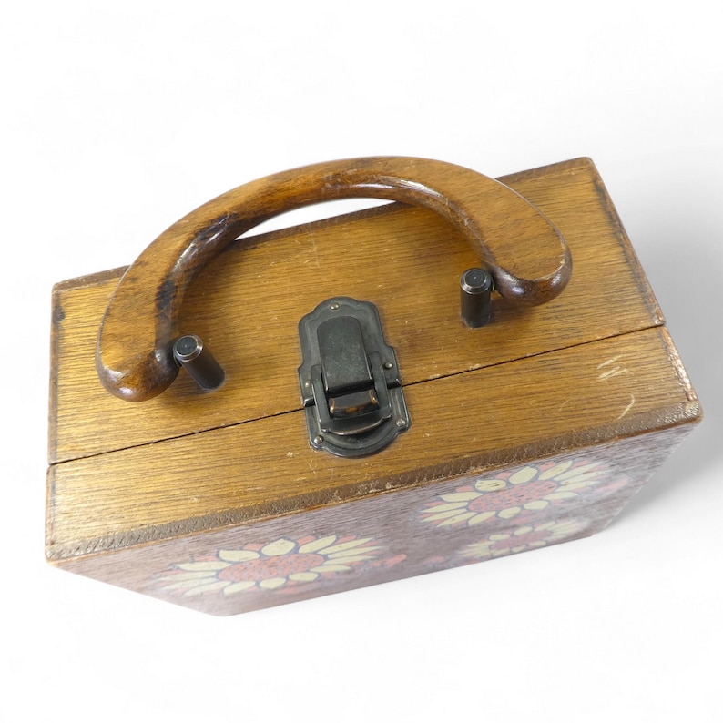 May include: A rectangular wooden box with a curved wooden handle and a dark metal latch. The exterior surface features a painted sunflower pattern with yellow petals and a reddish-brown centre, showcasing a natural wood grain finish throughout.