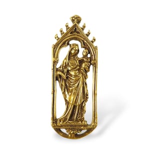 May include: A gold-coloured religious pendant depicting the Virgin Mary and child within an ornate, arched frame. The pendant showcases detailed craftsmanship and a design typical of religious art. The frame has a decorative top and base.