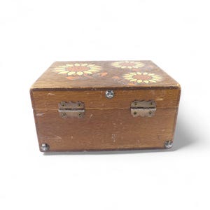 May include: A rectangular wooden box with a natural brown finish, featuring a painted sunflower design on the lid. The box includes two metal hinges on the back, a small metal latch on the front, and decorative metal studs on the bottom corners.