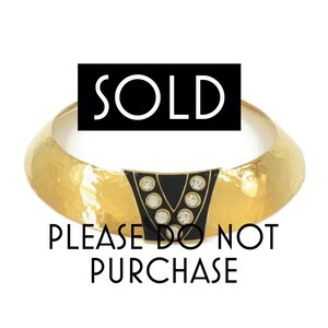 May include: A gold-toned hammered metal bangle bracelet featuring a central black V-shaped plaque adorned with clear round rhinestones. The image includes the text SOLD and PLEASE DO NOT PURCHASE overlaid on the bracelet design.