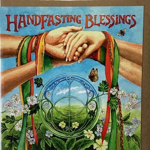 May include: A handfasting blessing card featuring a watercolour illustration of two hands clasped together, surrounded by green foliage, flowers, and butterflies. The text "Handfasting Blessings" is written in a decorative font at the top of the card.